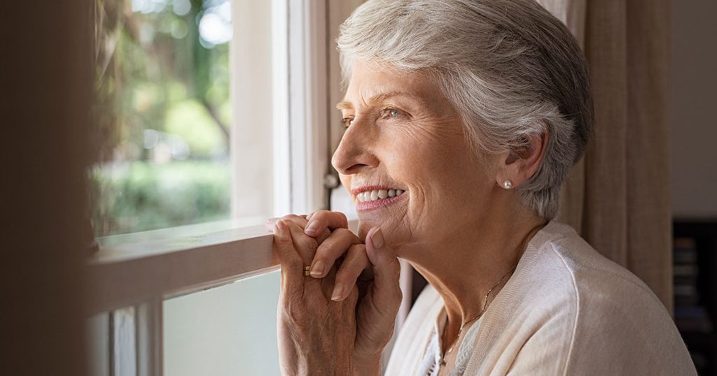 femme séniors souriante regardant par la fenêtre